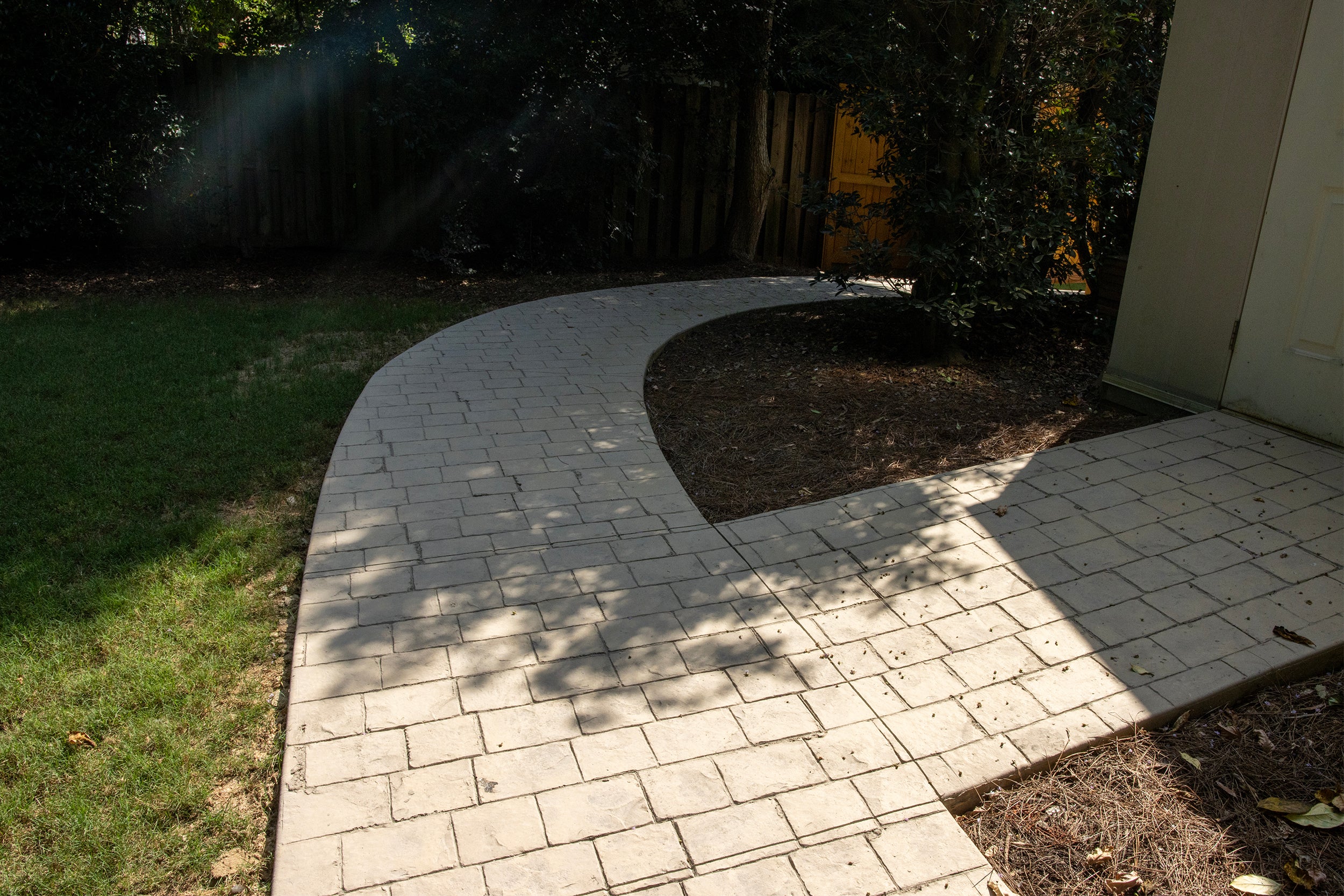 Curved brick pathway leading into a garden area with trees and grass.