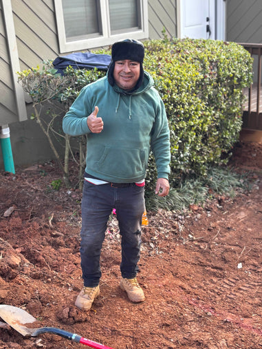 Man giving a thumbs up in front of a house with gardening tools around