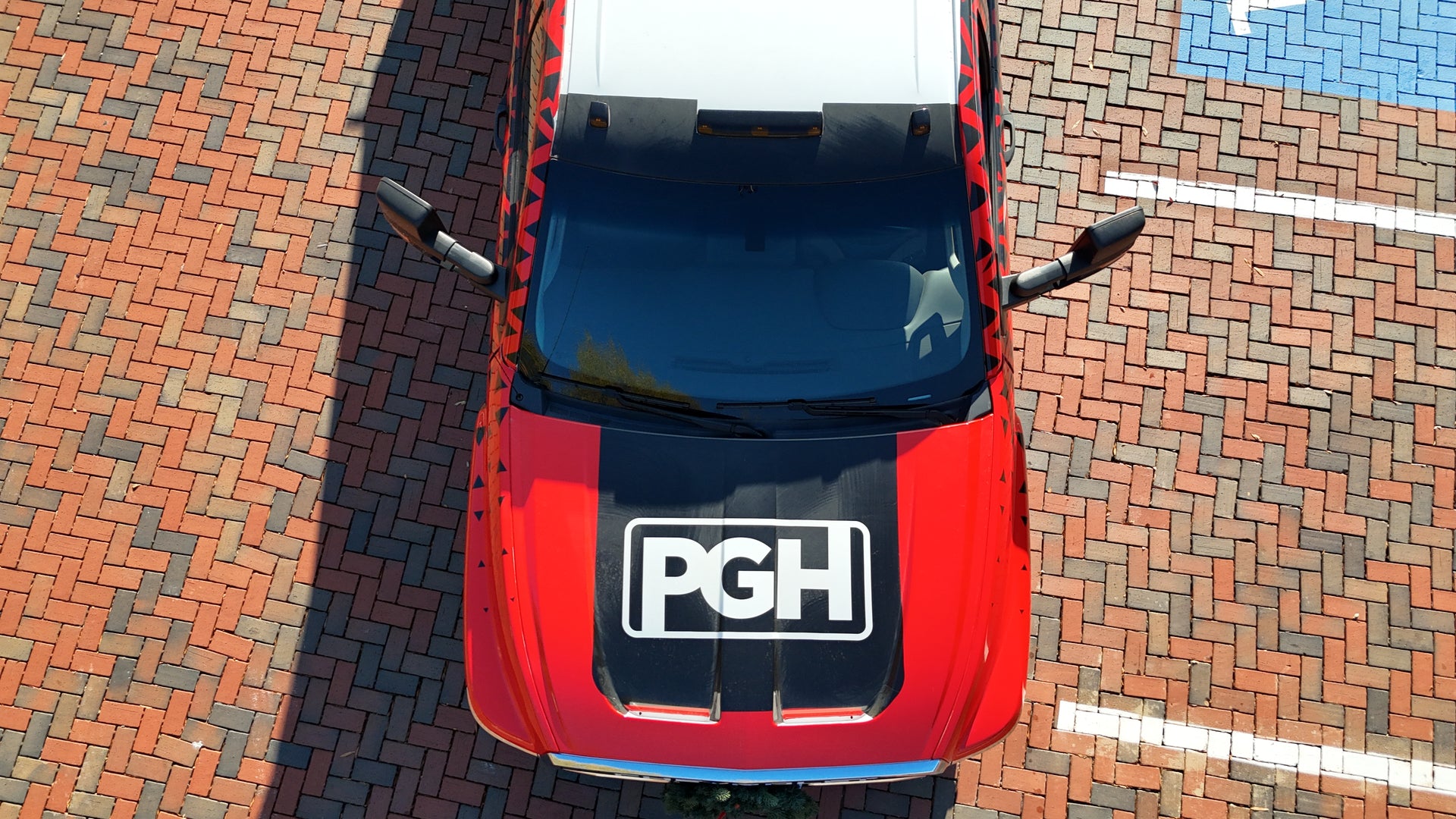 Red car with 'PGH' logo on a brick-paved surface