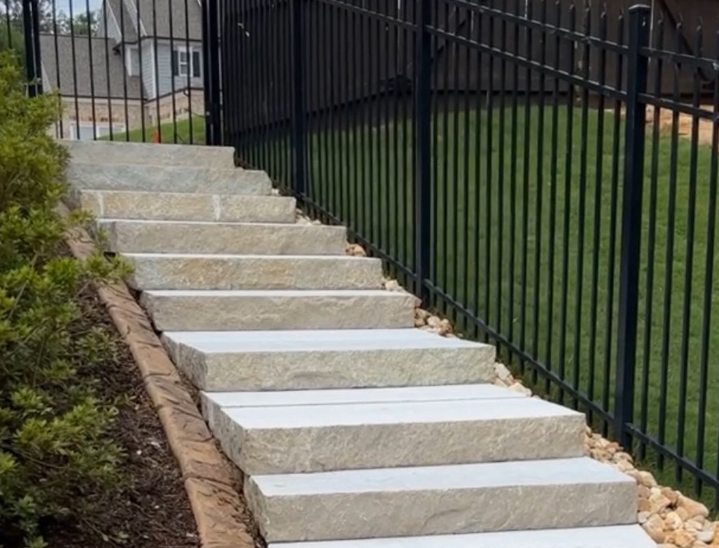 Stone steps leading up to a house with a black metal fence and grass in the background.