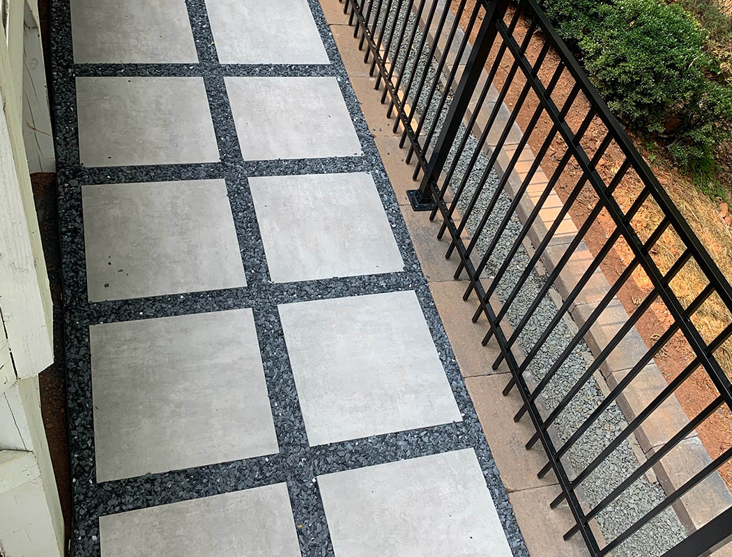Paved walkway with square tiles next to a black metal railing.