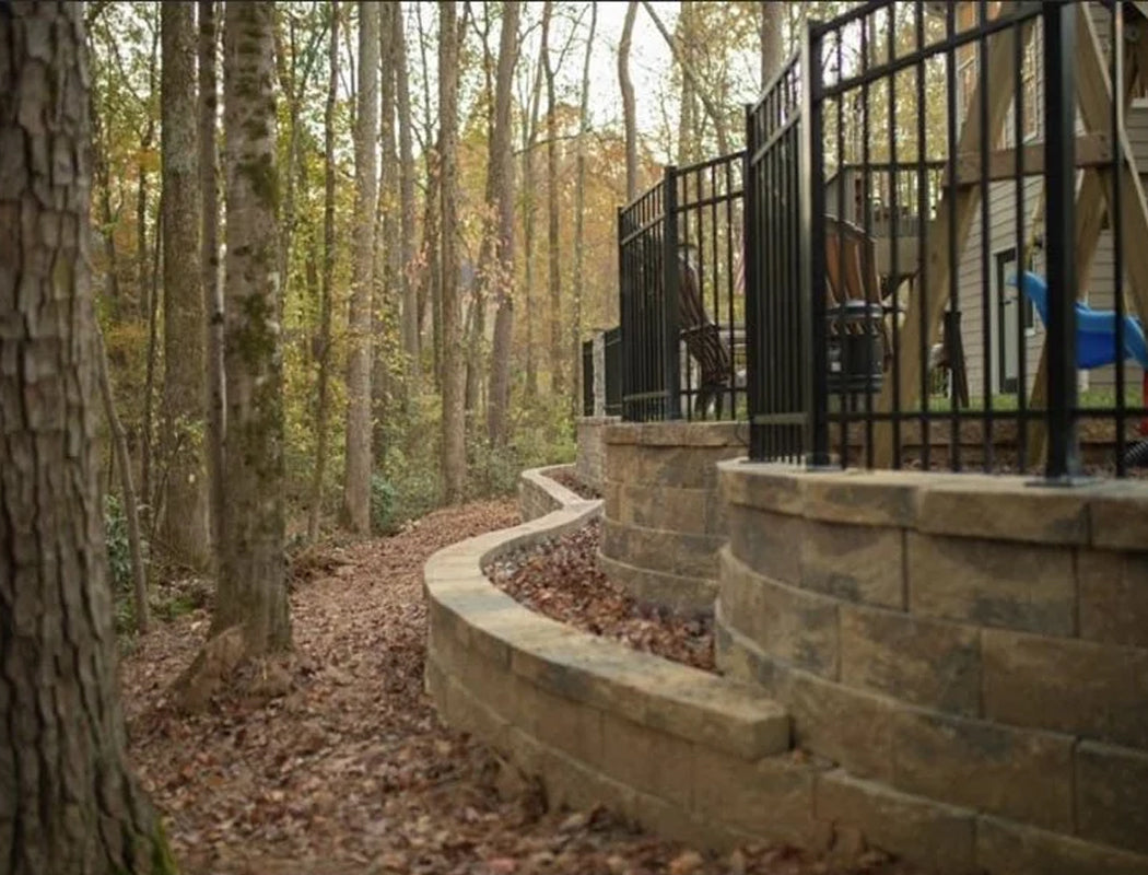 After transformation: gracefully curved multi-level natural stone retaining wall with wide capstone coping, creating safe terraced access and elegant backyard definition along a wooded path in Marietta, GA by Precision Grading & Hardscapes