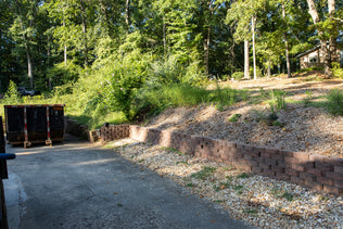 Outdoor area with a dirt path, trees, and a brick wall.