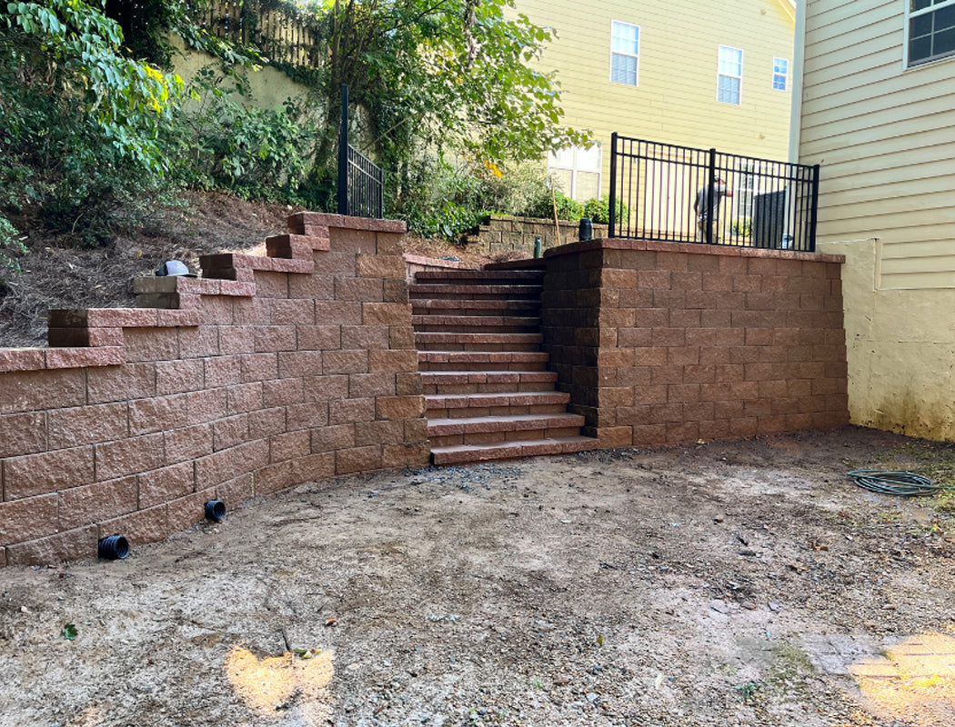 Brick retaining wall and steps leading up to a house with a yellow exterior.