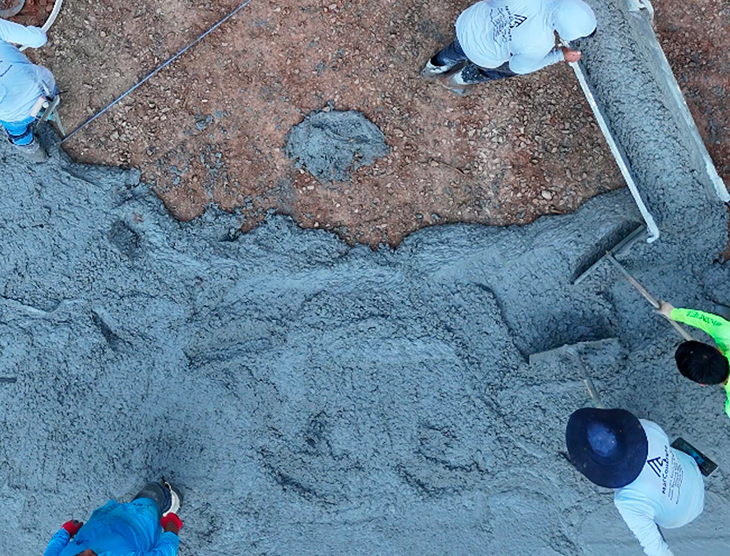 Precision Grading & Hardscapes crew actively finishing a concrete pour: team members using screeds, floats, and trowels to smooth and level fresh gray concrete during driveway installation
