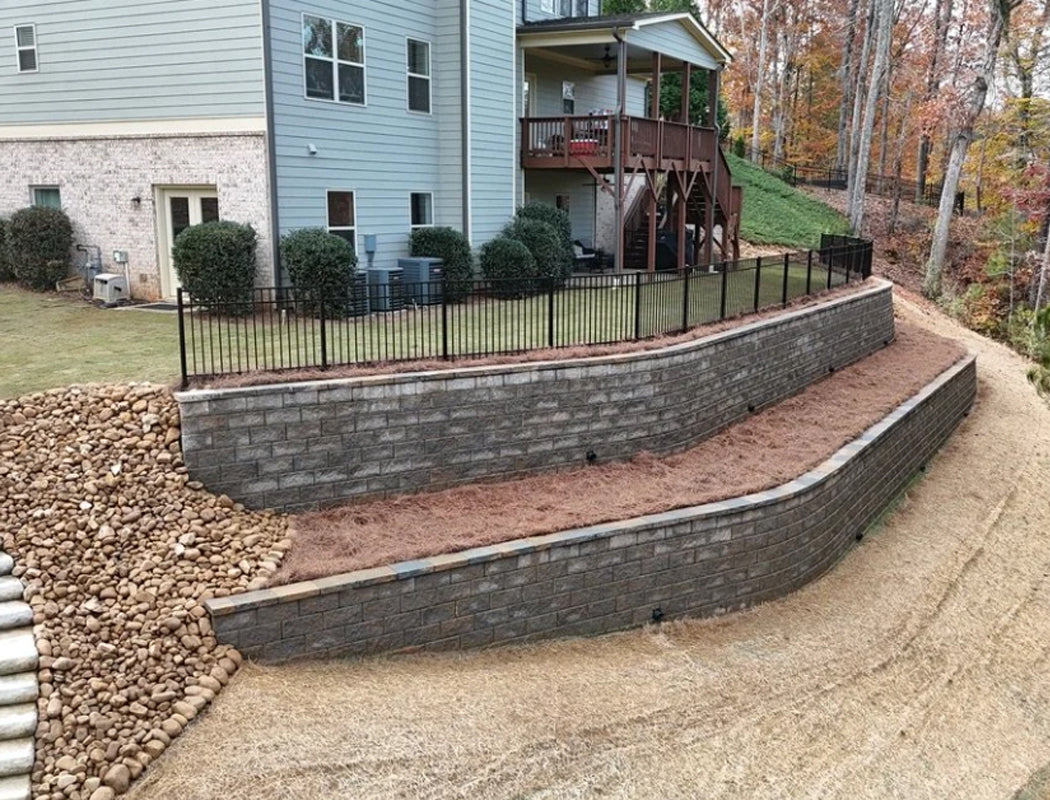 Precision Grading & Hardscapes custom retaining wall system with sweeping curves, black fence cap, and landscape grading transforming steep backyard slope in Marietta GA