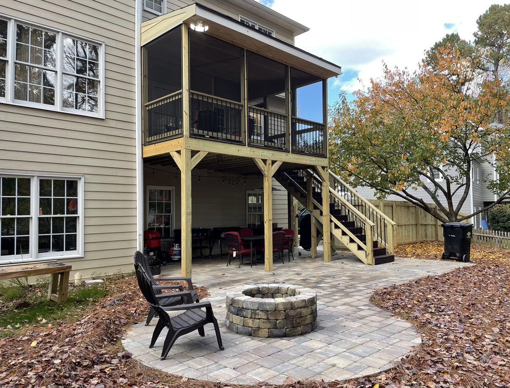 Cozy backyard retreat featuring custom stone fire pit surrounded by comfortable outdoor chairs, with elegant two-story screened porch addition – professional hardscaping and outdoor living space design in Marietta, GA by Precision Grading & Hardscapes
