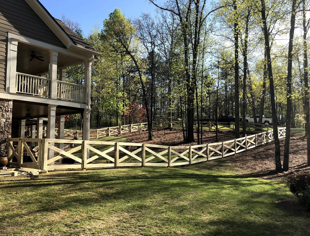 Elegant custom split-rail fencing with X-brace panels and wire mesh infill, gracefully curving around a large wooded backyard to define property lines and enhance natural beauty – professional fencing installation in Marietta, GA by Precision Grading & Hardscapes