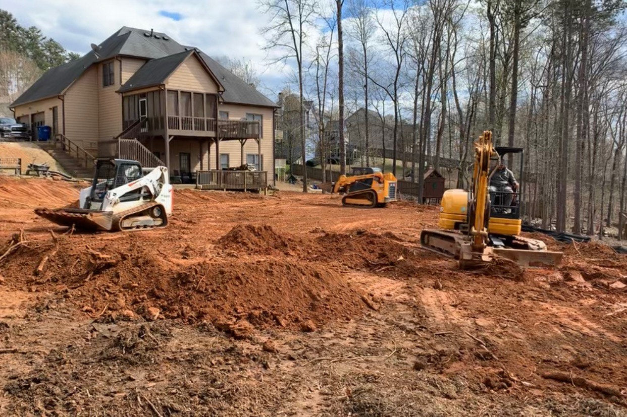 Construction site with excavator and loader grading in front of a house