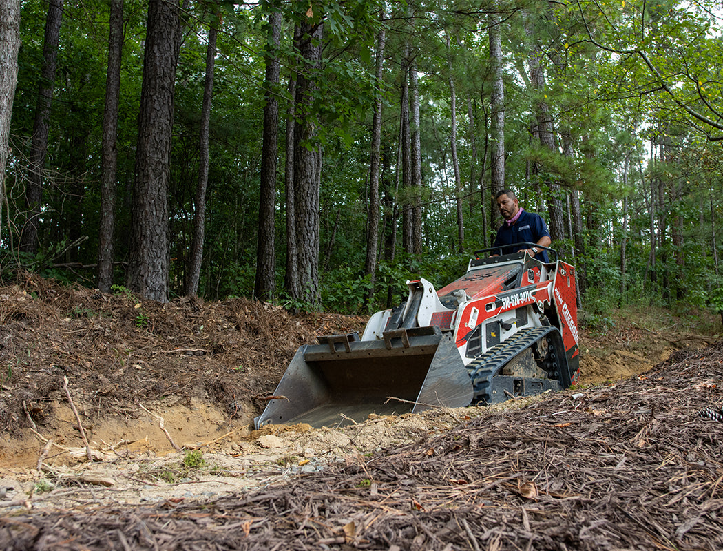 Person operating a small excavator in a forested area