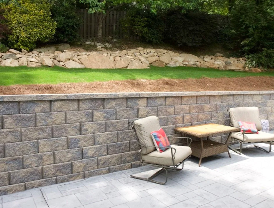 Cozy outdoor seating area with cushioned chairs and side table on custom gray paver patio, backed by sturdy segmental retaining wall and natural boulder slope