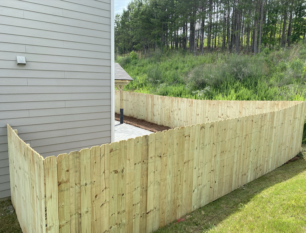 New wooden fence featuring tall scalloped-top panels curving gently around a residential yard, providing privacy and definition near pine trees and natural terrain in Marietta, Georgia