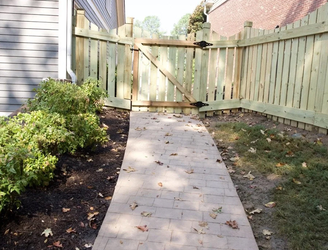 Paved pathway leading to a wooden gate with plants on either side.
