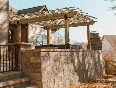 Outdoor kitchen with retaining wall and wooden pergola on a clear day