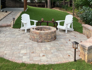 Backyard with stone fire pit, white Adirondack chairs, and paved patio.