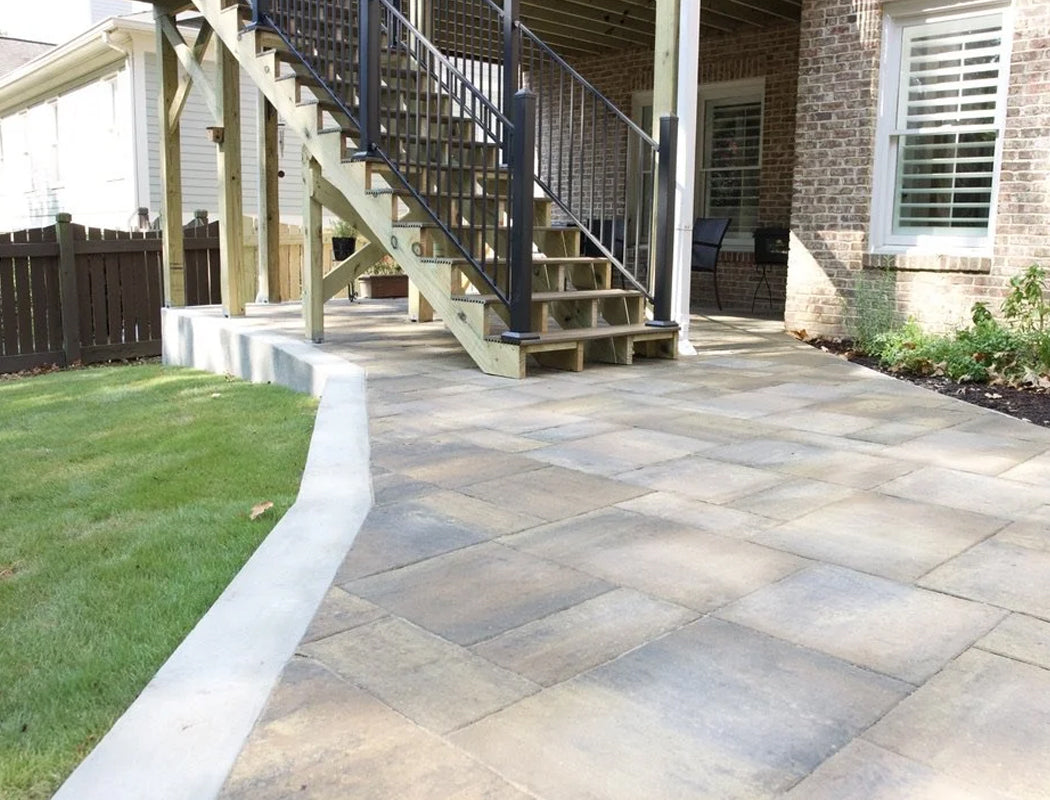 Elegant natural stone paver patio installation bordering elevated porch with timber supports and black railing, creating seamless backyard transition in Marietta, Georgia
