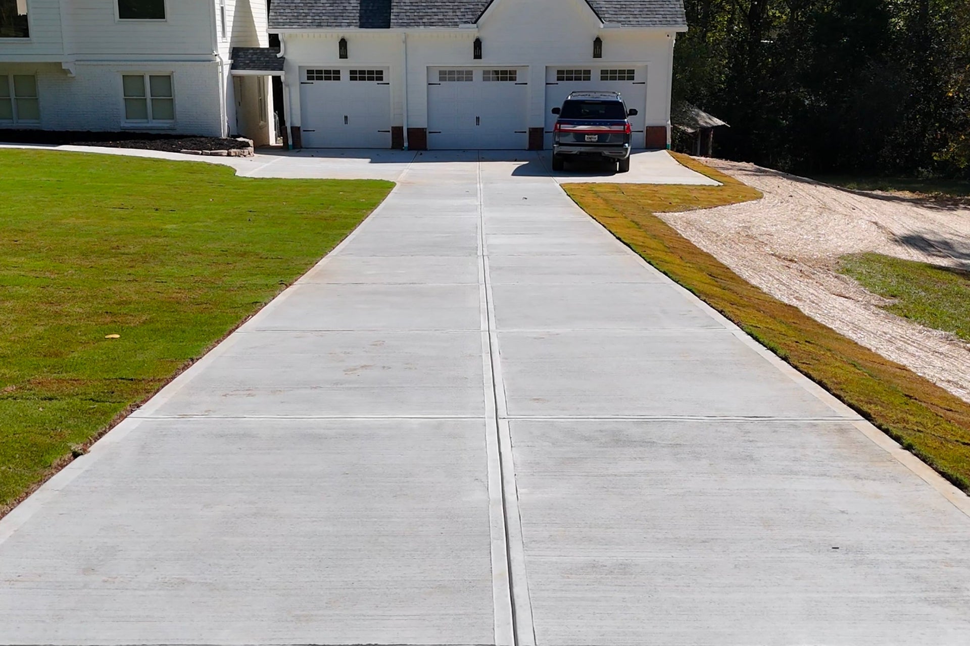 Fresh concrete driveway leading to a house with a grassy area on either side.