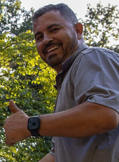 Man giving a thumbs-up gesture outdoors with trees in the background