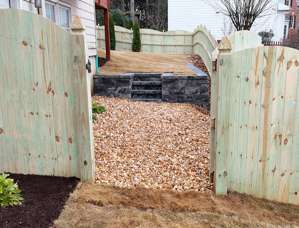 Premium wooden gate open to a gravel driveway with steps leading up to a backyard.