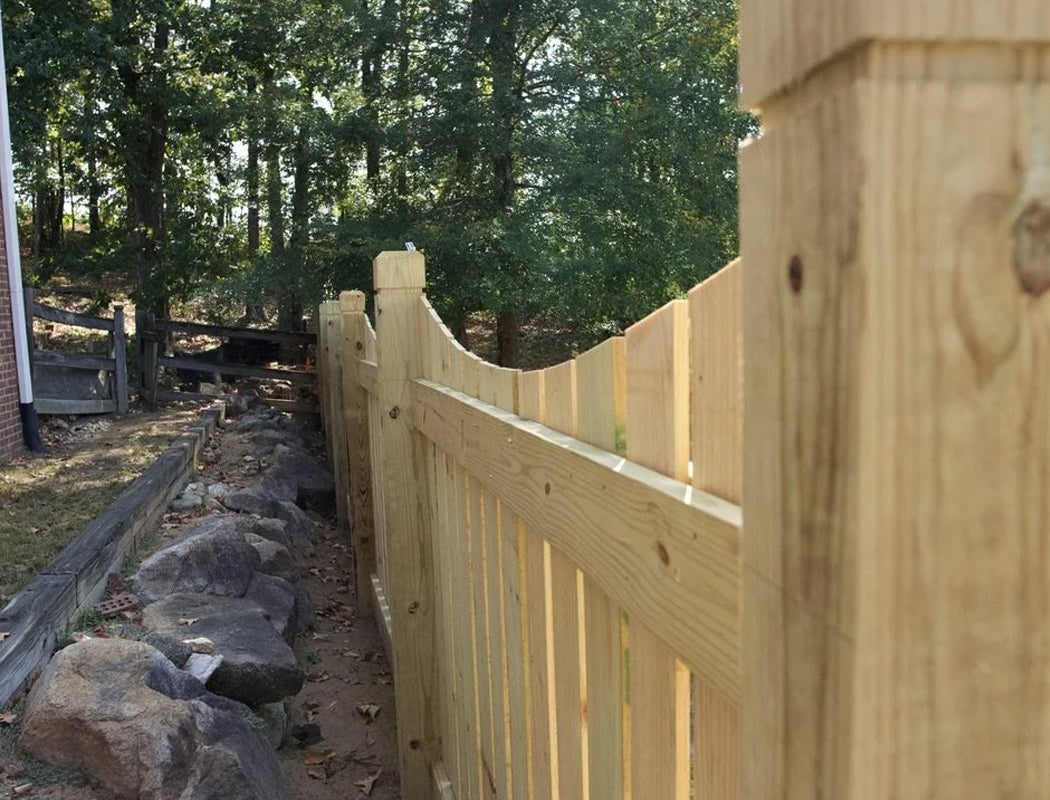 Newly built wooden fence featuring scalloped pickets, tall posts with caps, and precise alignment beside a natural rock-lined drainage channel in a wooded backyard setting in Marietta, Georgia