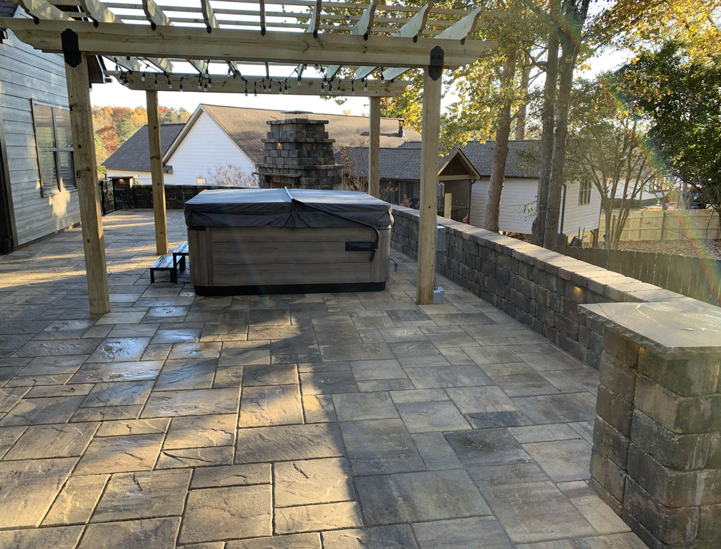 Luxurious stamped concrete patio featuring pergola, hot tub placement, built-in stone fireplace, and low retaining wall for elevated backyard views in Marietta, Georgia