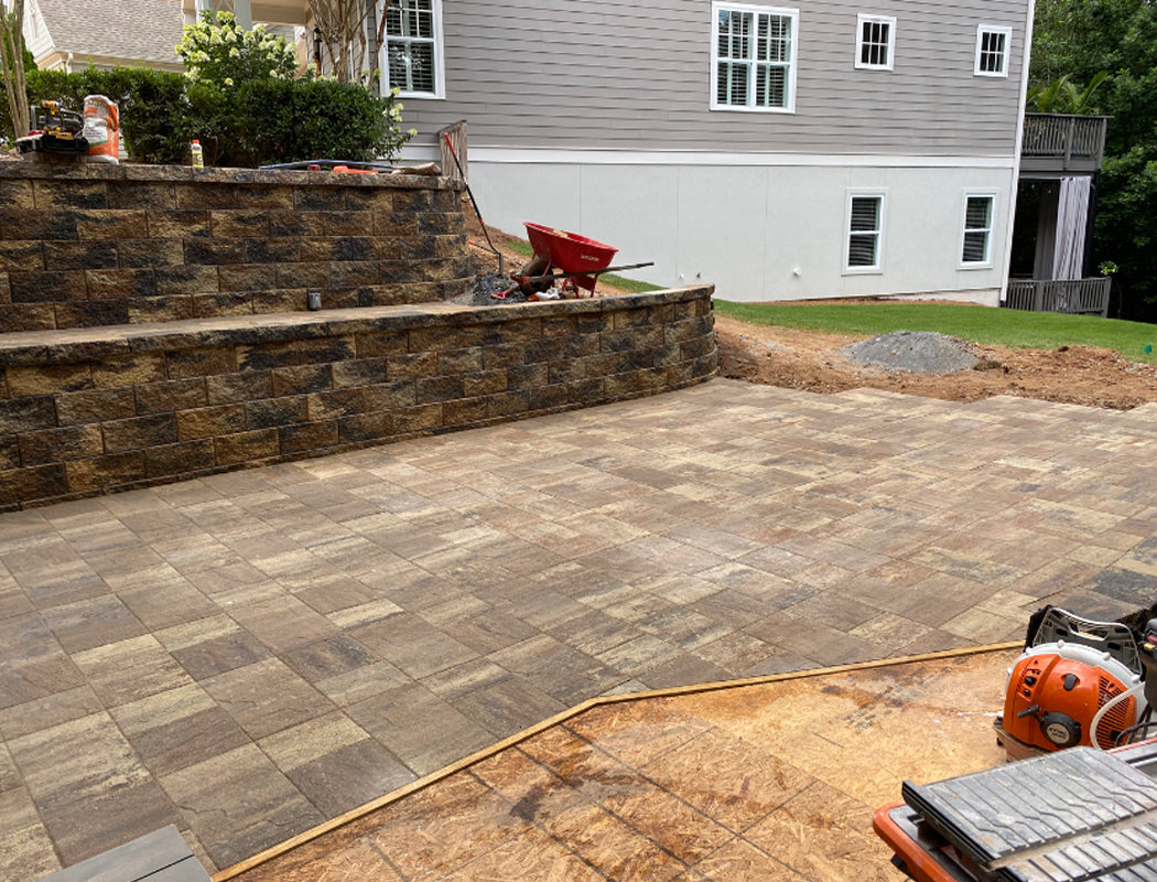 Construction phase of luxurious stamped concrete patio featuring large-format textured slabs, multi-tier retaining wall foundation, and heavy equipment grading in Marietta, Georgia