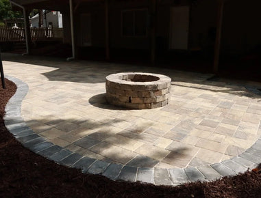 Fire pit surrounded by a circular stone patio in an outdoor setting.