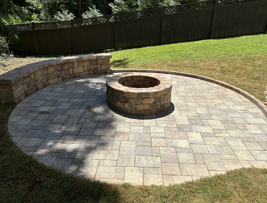 Stone fire pit in a circular patio area with grass and trees in the background