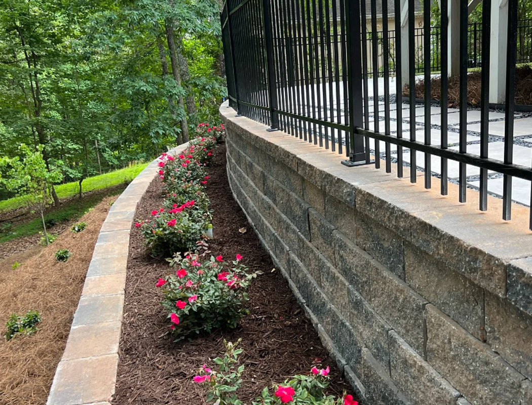 Stone retaining wall with black metal fence and garden bed with pink flowers