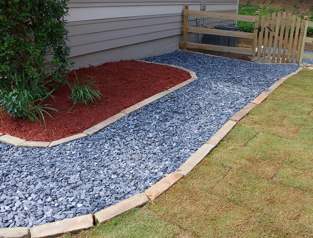Garden bed with red mulch and blue gravel walkway next to a house.